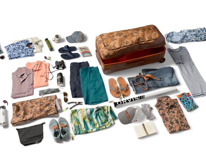 A wide assortment of travel clothes and shoes with a suitcase