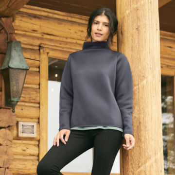 Woman in Carbon Mockneck Sweatshirt leans against a support beam.