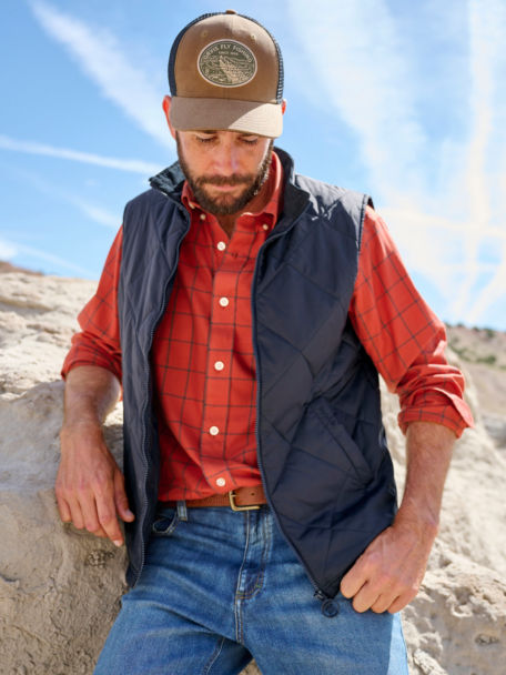 Man wears a button down, vest, and blue jeans