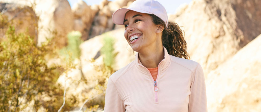 A woman hikes in the Rocky Mountains wearing a pink quilted sweatshirt and capA woman hikes in the Rocky Mountains wearing a pink drirelease sweatshirt and cap