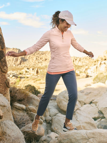 Woman in Blush Horseshoe Hills 1/4 Zip Sweatshirt walks down a rocky trail in the desert.