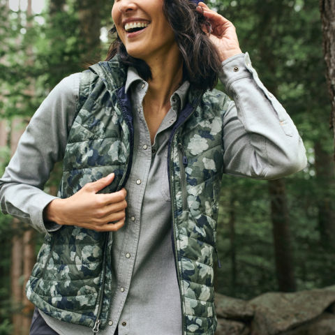 A model smiles while wearing a green button-down shirt and camo quilted vest