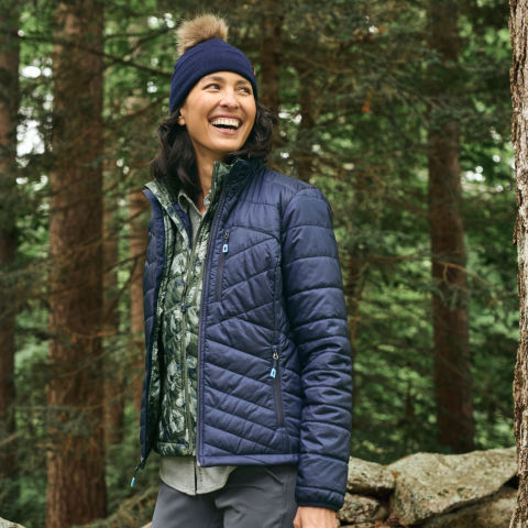 A model in a navy quilted jacket and hat poses in the forest