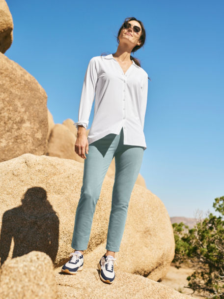 Woman in White Elevated Tunic Button Down and Tidewater Flex Day Natural Fit Straight Leg Ankle Pant stands on a desert rock.