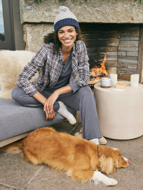 Woman in Gray/Harvest Gold Plaid  Soft Flannel Big Shirt relaxes next to a fireplace with her dog.