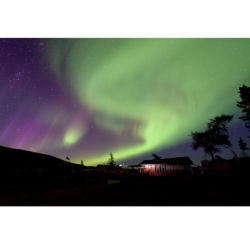 A dramatic photo of West Hills Lodge with the swirling purple and green sky of an aurora borealis.