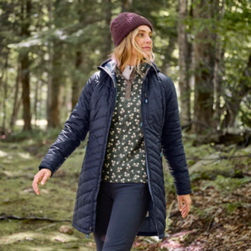 Woman in recycled drift parka walks through the woods.