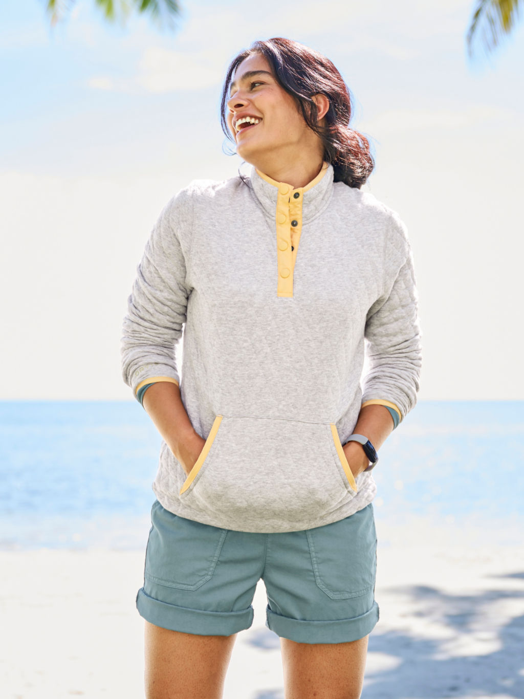 A woman wearing a light gray quilted sweatshirt and sunwashed teal shorts.