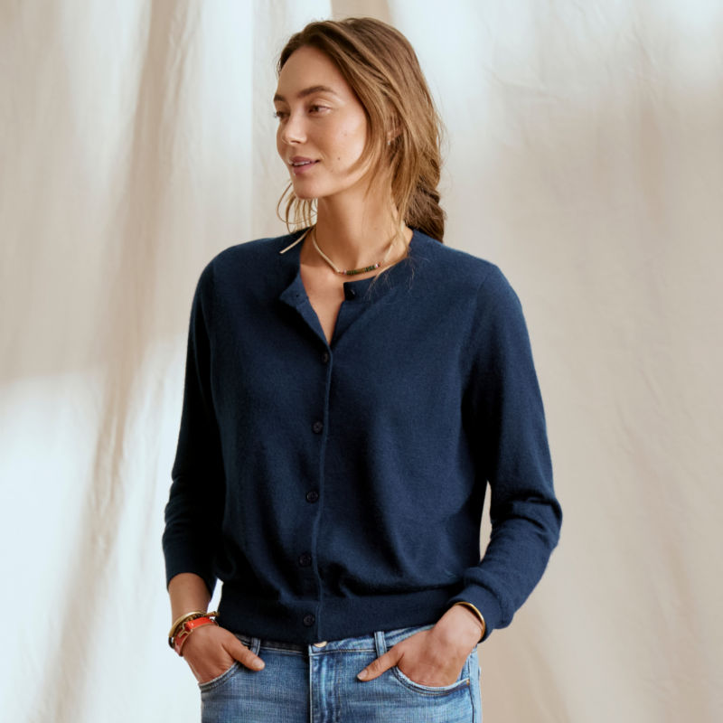 A model stands in front of a dropcloth wearing a navy cashmere cardigan.
