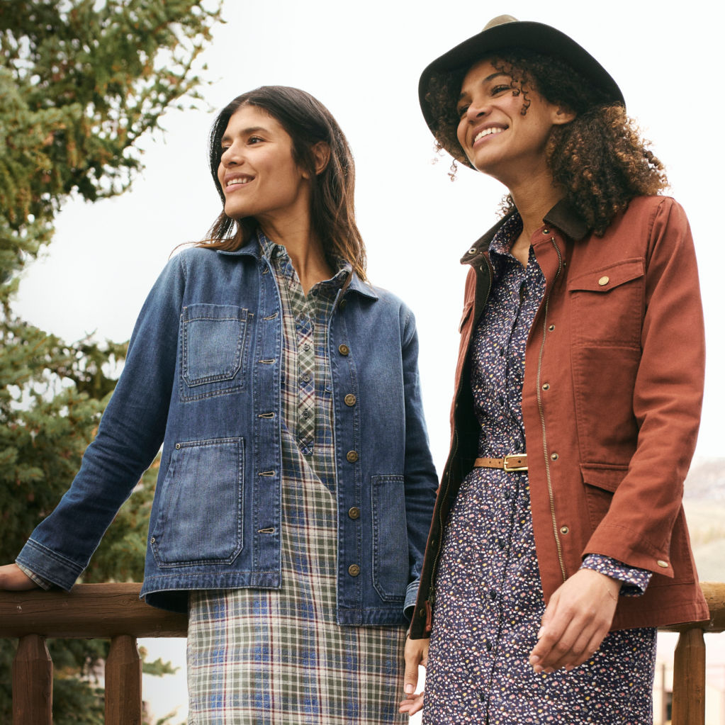 Two women look on from atop a deck.  Both are wearing jackets and dresses.