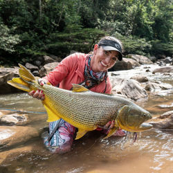 A woman kneeling in a river holding a very large fish