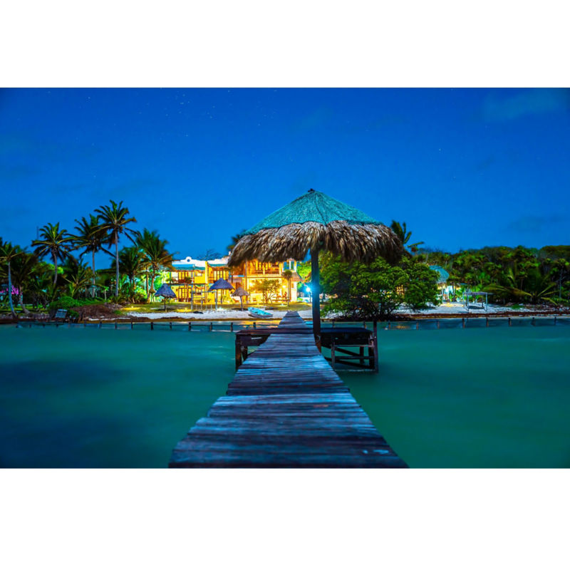 Looking down a dock at beautiful lodge that's lit up at night.
