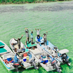 A large group of people with their hands up in the air standing on boats over green water.