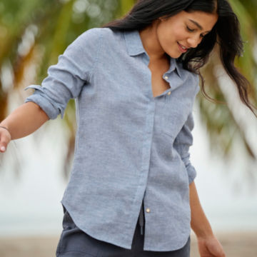 Woman in Performance Linen Long-Sleeved Shirt sits on a beach.