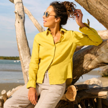 Woman in Performance Linen Long-Sleeved Shirt leans on some driftwood.
