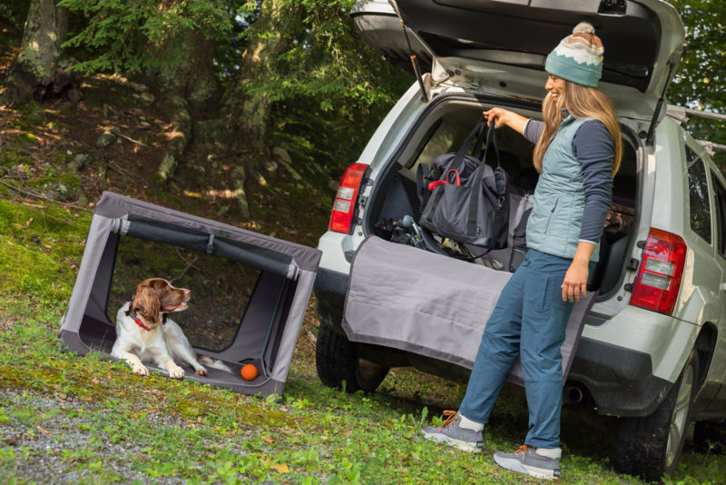 Dog laying in a travel crate while his owner is organizing the cargo space of their car.