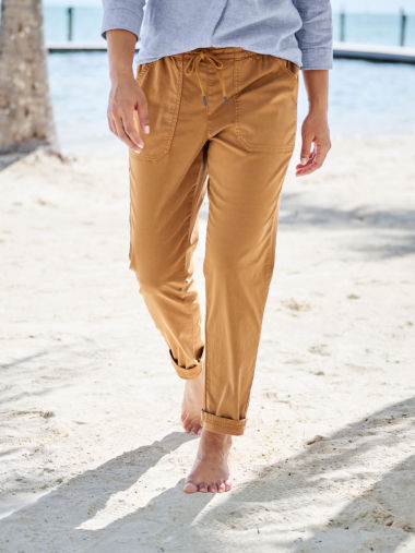 A waist-down view of a woman walking on a beach wearing gold pants.