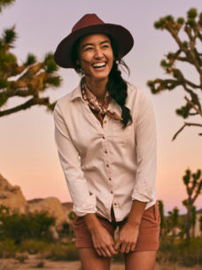 A model in orange shorts and a button-down shirt laughs in the desert
