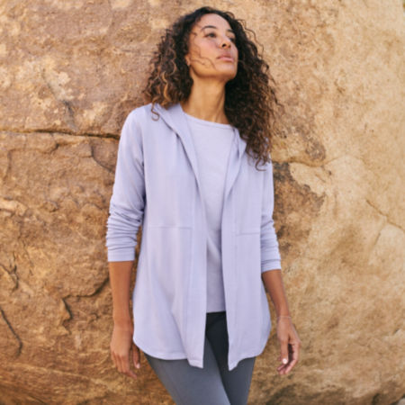 A woman wearing a lavender Odyssey Cardigan Sweatshirt while leaning against a large rock