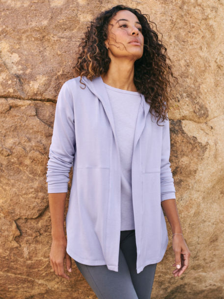 Woman in Thistle Odyssey Cardigan and Ribbed crewneck shirt leans against a rock in a desert park.
