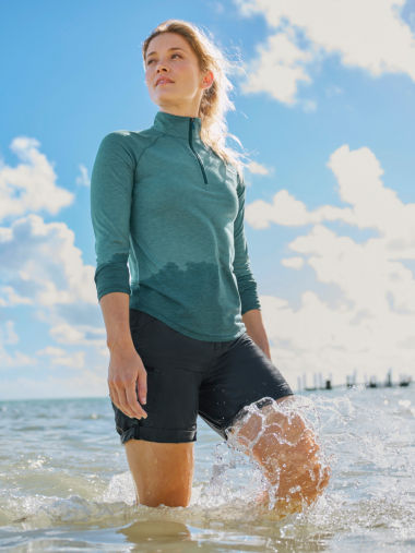 A woman standing by the ocean wearing a green DriCast™ Quarter-Zip.