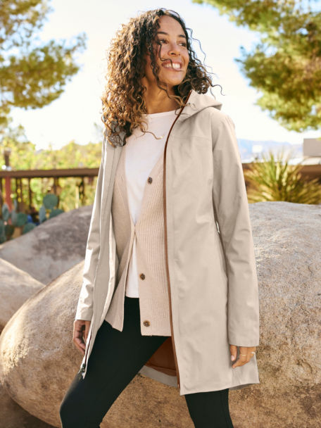 Woman wearing Anywear Relaxed Cardigan and Ultralight City Jacket walks through a rock park in the desert.