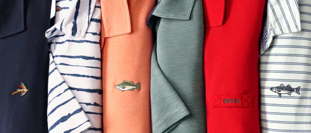 A collection of Orvis polo shirts in a variety of colors laid on a table.