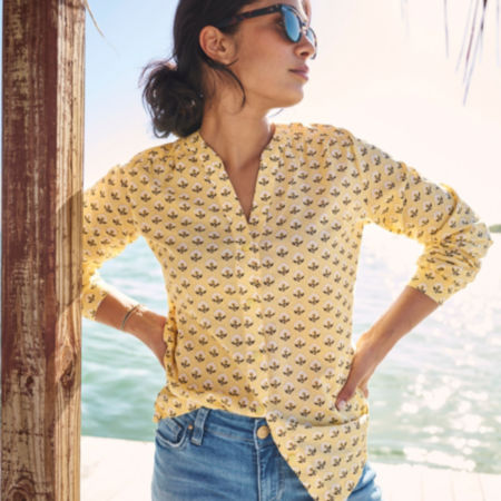 A woman wearing a yellow printed long-sleeved button down shirt, standing on a tropical beach