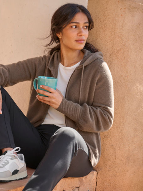 Woman in Boiled Cashmere hoodie takes her coffee while sitting down on a porch.