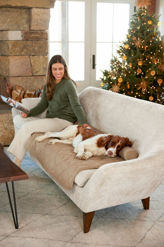 A woman and her spaniel relac on a light cream couch with an Orvis furniture protector.