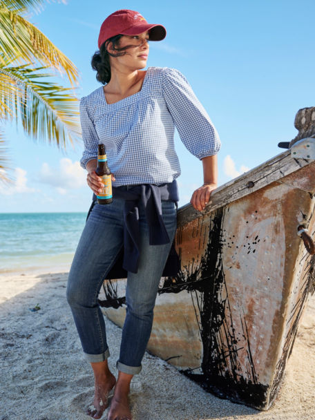 Woman wearing jeans on the beach leaning on an old boat