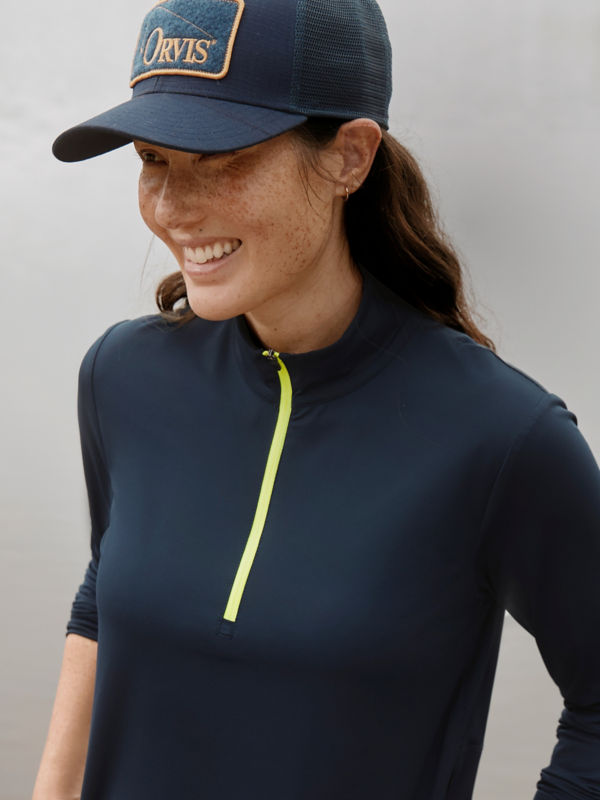A smiling hiker pauses wearing a navy sun protective quarter-zip with a navy Orvis ball cap.