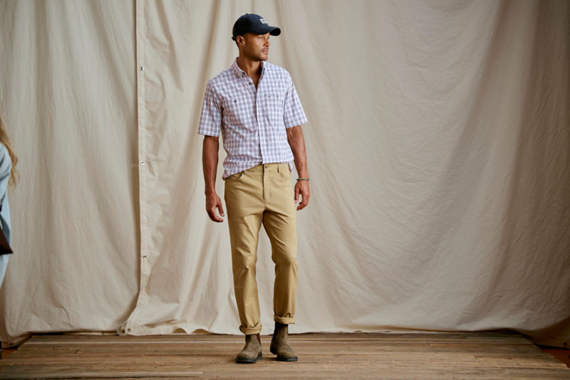 A model wearing a plaid short-sleeve shirt tucked into slim khaki pants.