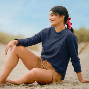 Woman in Riverside Crew sweatshirt sits on the beach.