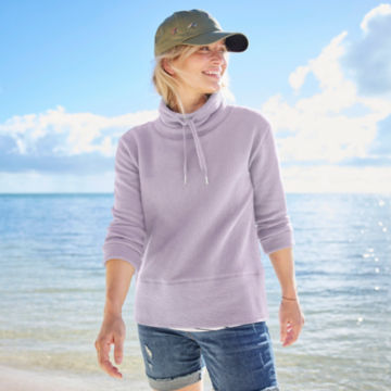 Woman in textured cowl sweatshirt walks up from the shoreline.