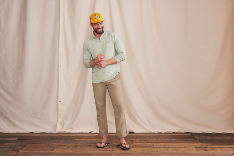 Model is wearing a light green sun protective quarter-zip, tan pants, and a yellow hat.