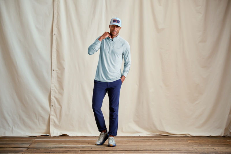 A model with his hand in his pocket wearing an Orvis baseball hat and a hooded performance shirt.