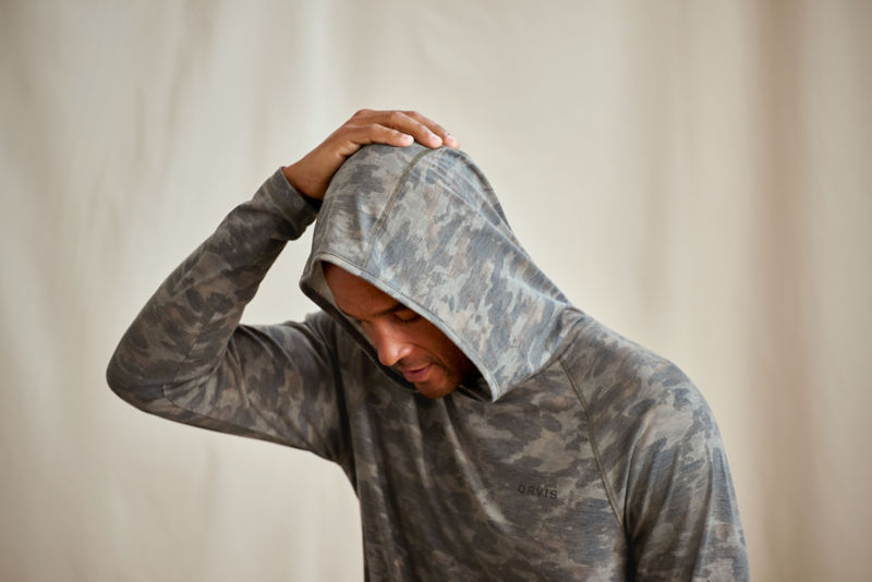 A model wearing a softly-grayed camo hoodie with his hand on his head.