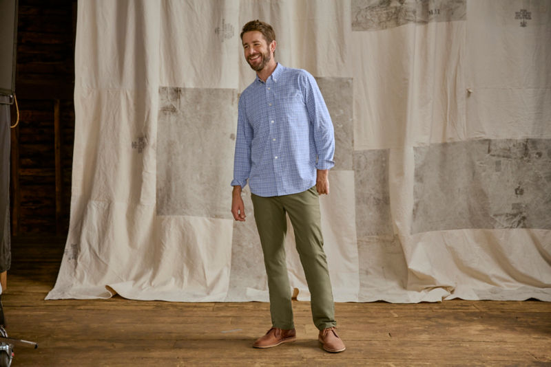 Man wearing blue plaid shirt and green pants in a studio.