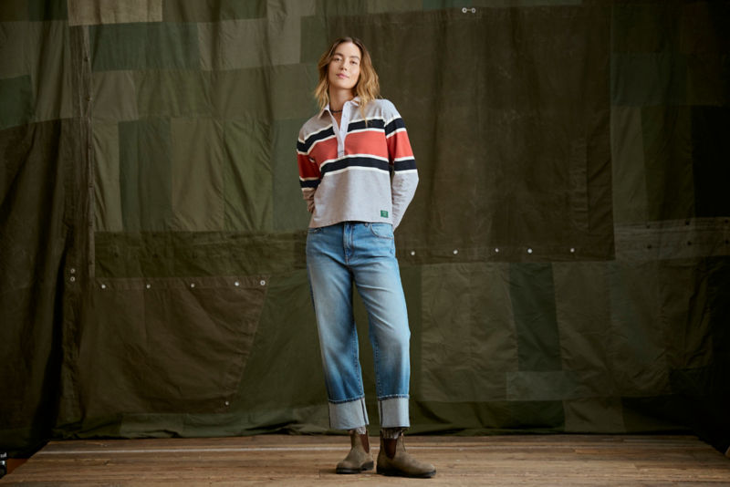 Woman wearing striped rugby shirt and jeans in a studio.