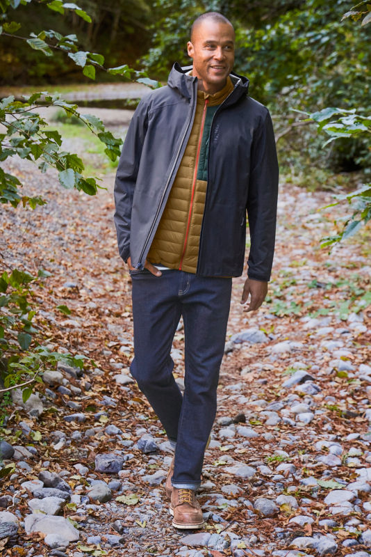 A man pauses on a trail while wearing a navy rain jacket over a gold and green drift vest.