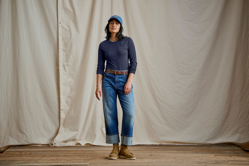 Woman wearing navy long sleeved tee and jeans in a studio.