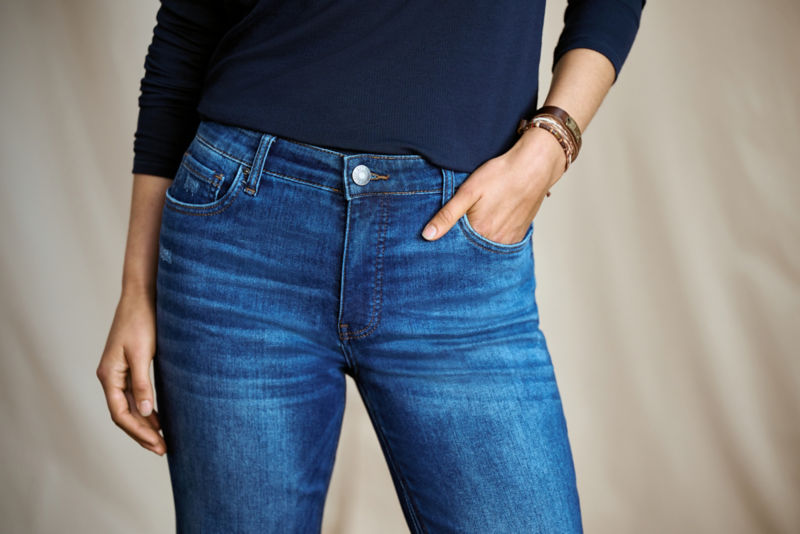 A waist-down view of a person wearing a long-sleeve navy tee tucked into blue jeans.