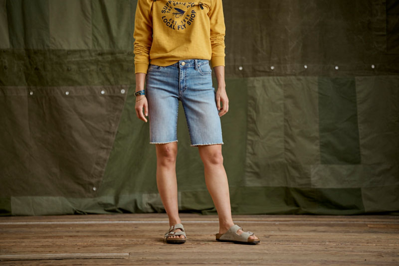 A close-up of a model wearing cut off jean shorts and a yellow sweatshirt.