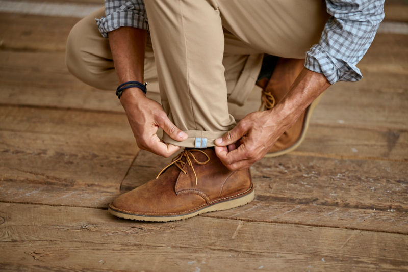A man squats down to adjust his pants cuff over his leather boots.