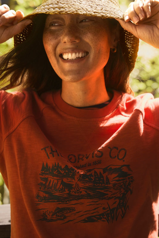 A model wearing a red graphic print sweatshirt and straw hat.