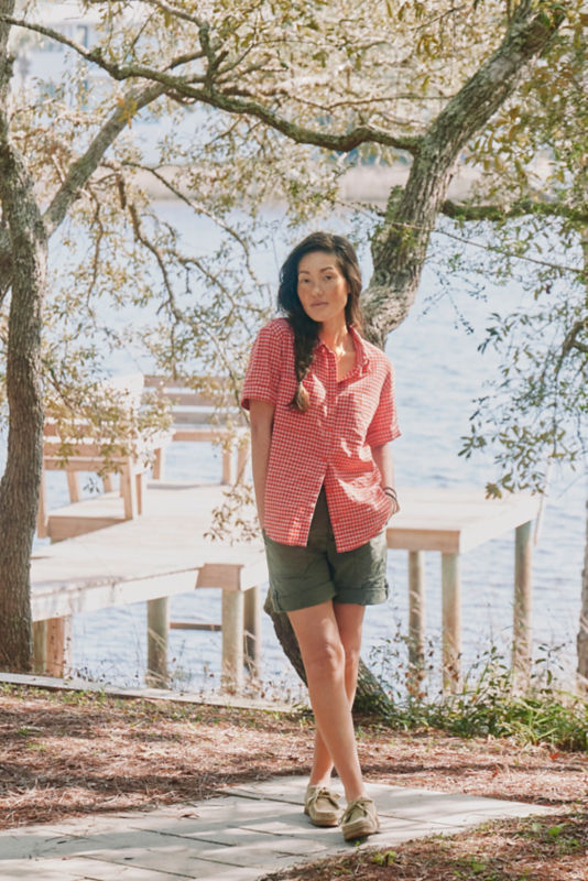Woman wearing red plaid shirt and green shorts standing in front of a dock.