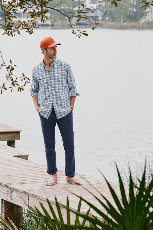 A waist-down view of a model wearing a blue pants on a wooden dock.