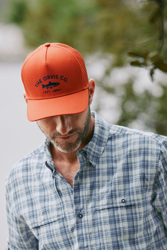 A model wearing a blaze orange ball cap with a fish embroidered on it.