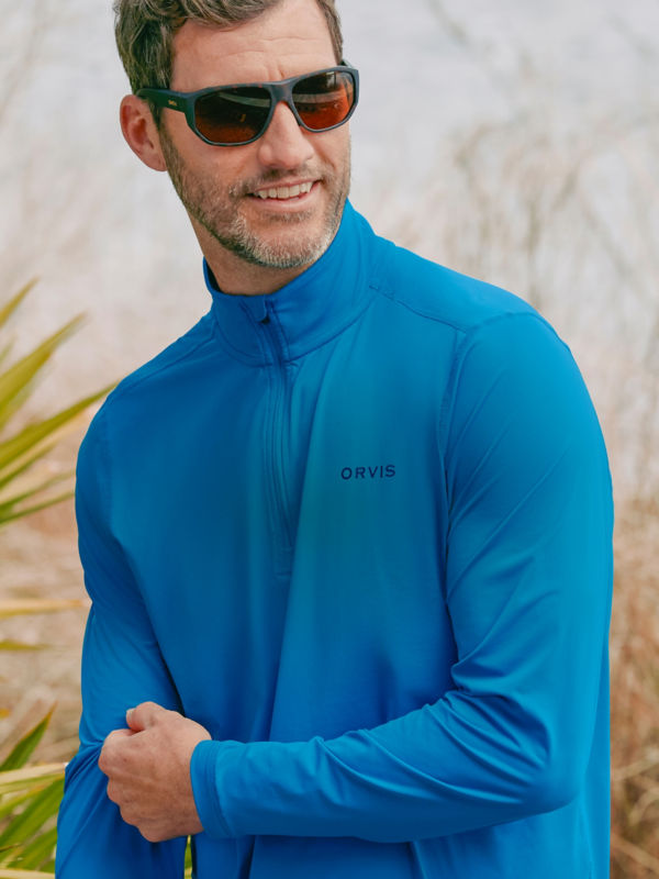A smiling hiker pauses to pull up the sleeves of his blue sun protective shirt.